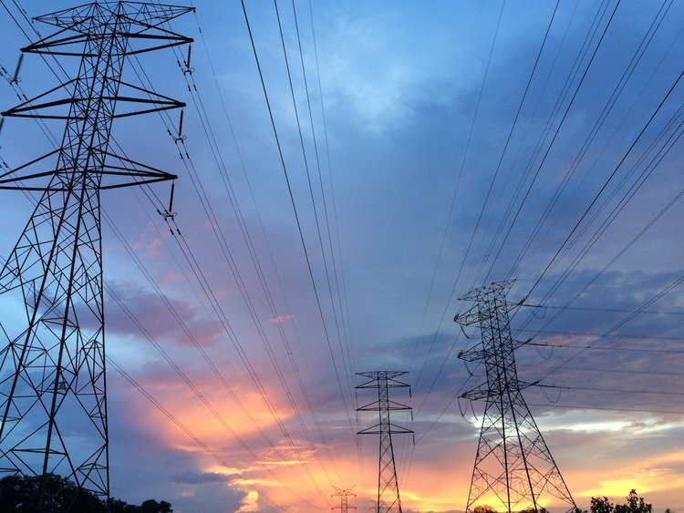 Electricity pylons against a cloudy sky with a sunset