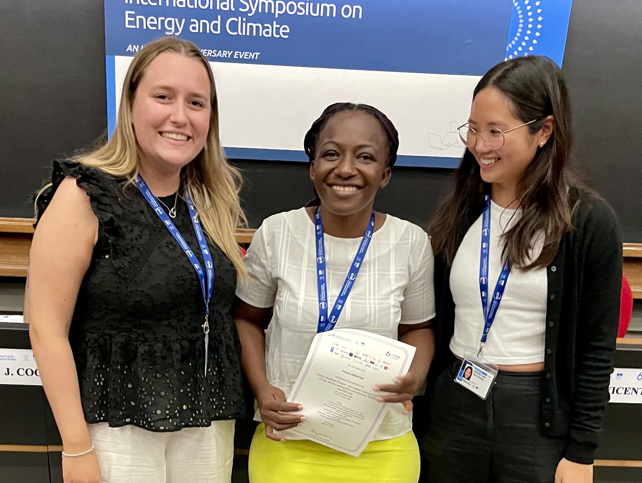 three smiling women, one with a certificate