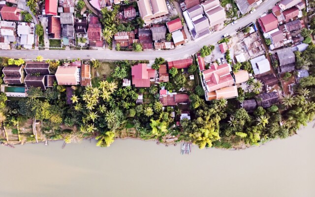Aerial shot of a village by a river, with green trees and red roofs.