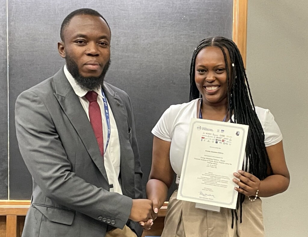A black woman with long hari and a white top receives a certificate from her male trainer.