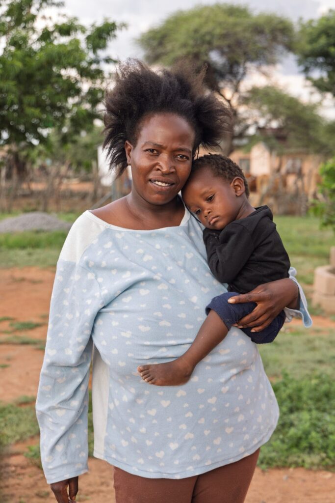 An African Mother in a light blue top is holding her toddler close to her, in one arm