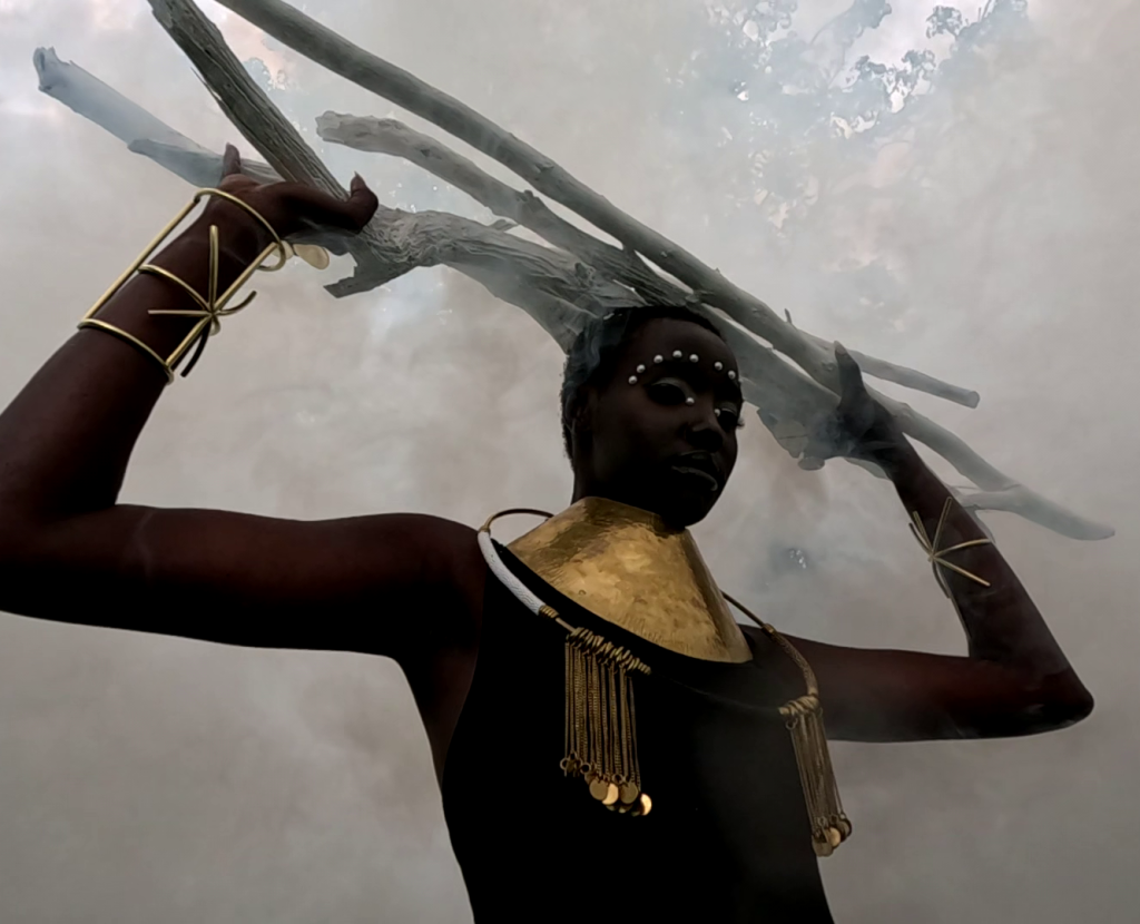 A still from the film 'Smoke Jumpers". The image depicts a woman wearing ornamental jewellery holding sticks above her head. The scene is smokey.
