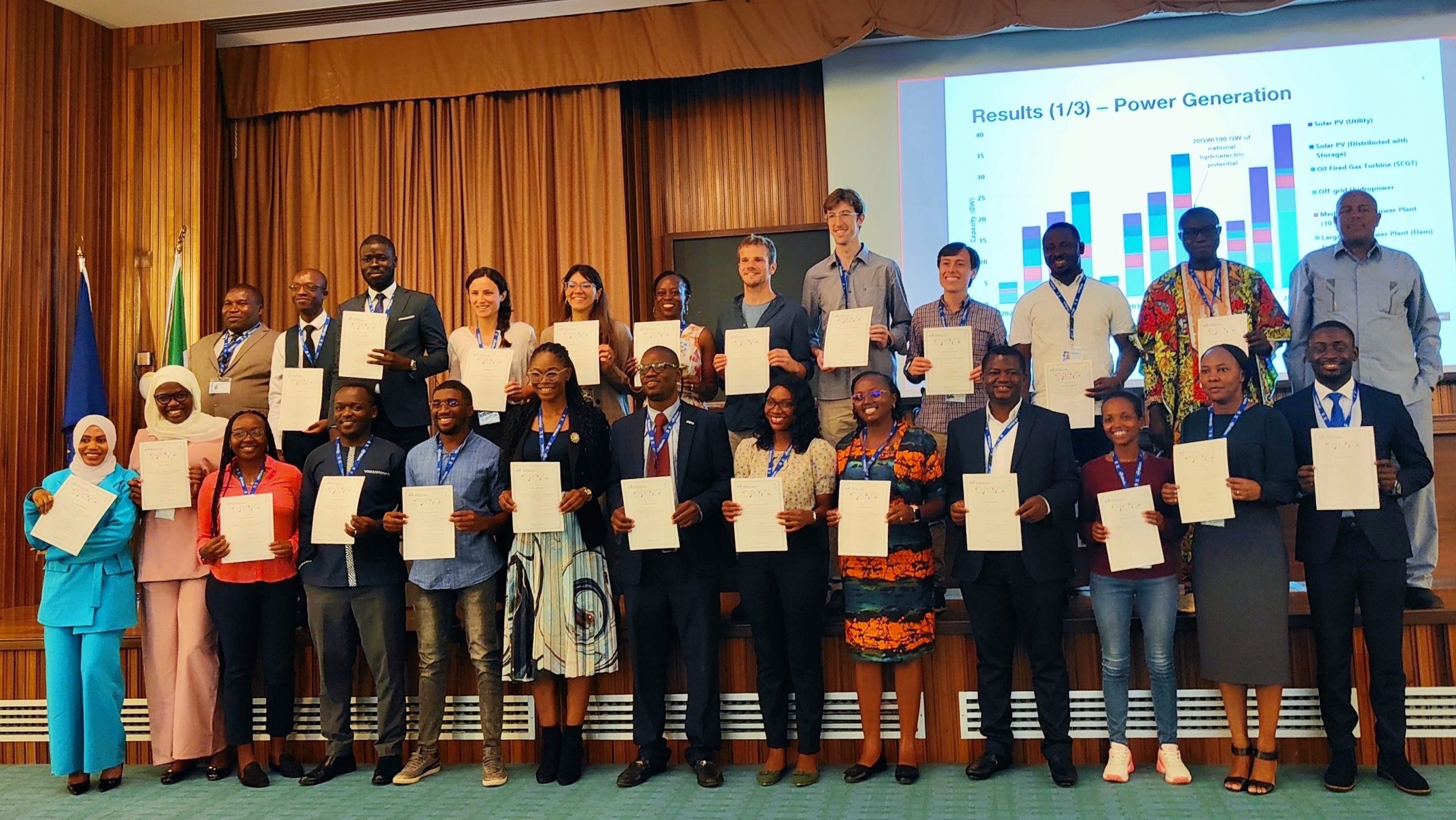 A large group photo of participants holding their certificates of completion. Taken in July 2023 at the ICTP Joint Summer School on Modelling Tools for Sustainable Development (now called EMP-Global), in Trieste