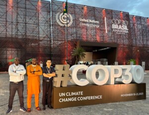 Three men standing next to a white sign saying 'COP30'