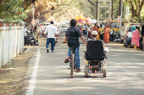 Cochin, India - January 1, 2016: Young boy on wheelchair walking with his friend on the street. Concept - strong friendship between healthy and disabled boy